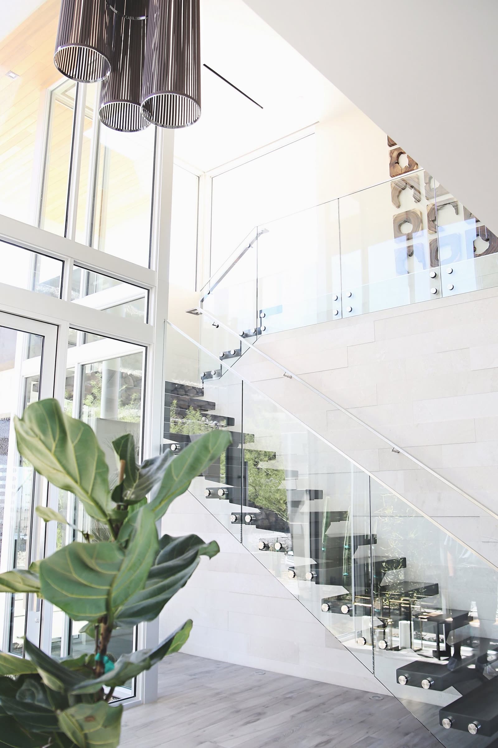 A glass-railed staircase rising through a double-height entry in a Widespread custom home